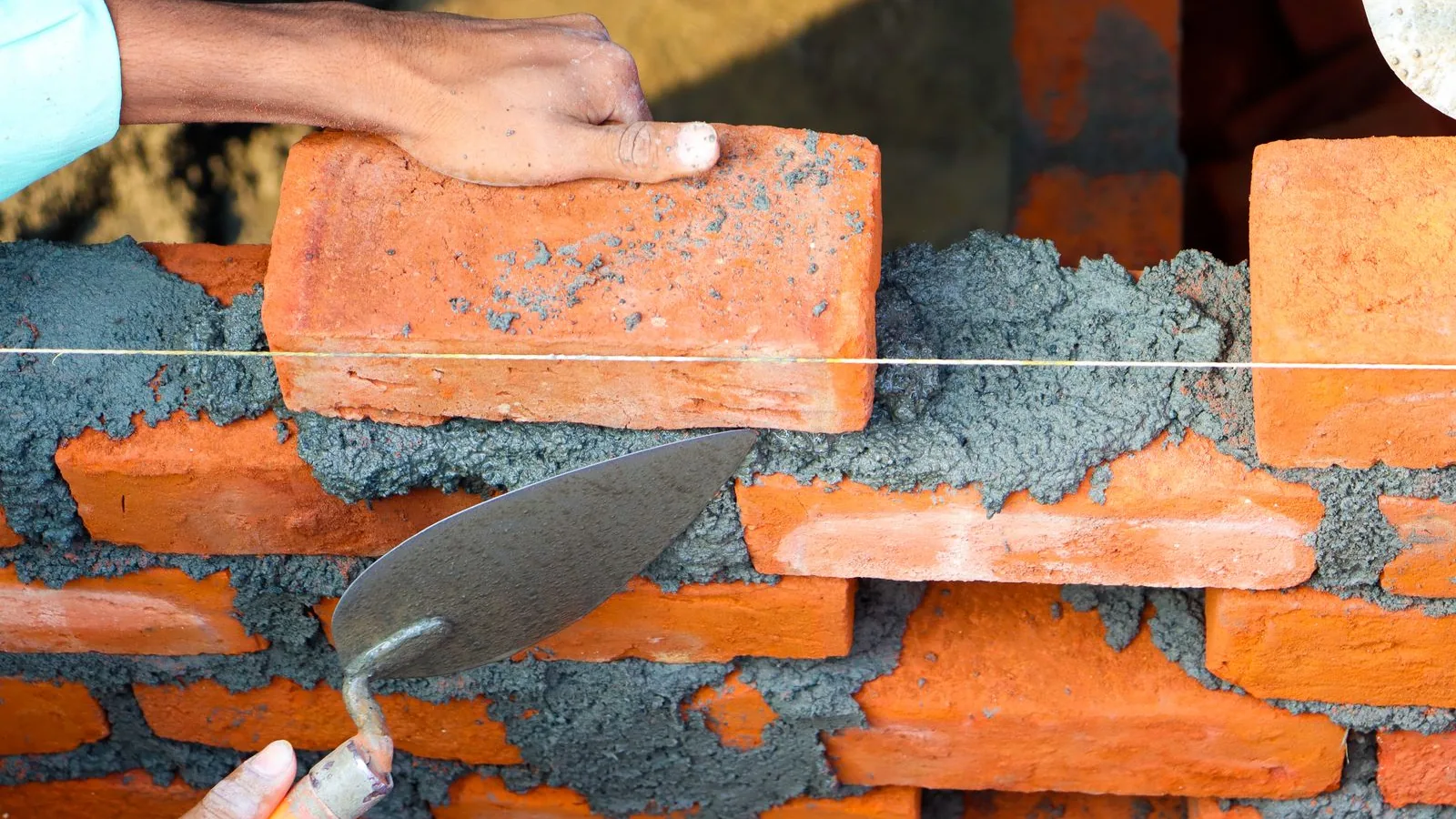 A bricklayer bedding a brick into mortar, level with a taut string line